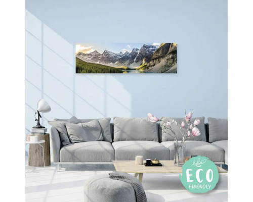 Obývací pokoj s pohovkou a nástěnnou malbou horské krajiny s jezerem. Na stole je váza s květinami. Označení: Šetrné k životnímu prostředí.