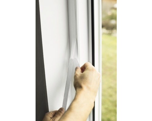 Osoba připevňuje těsnicí pásku k rámu okna.