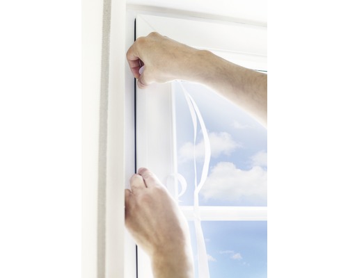 Ruce připevňují těsnicí pásku k rámu okna.