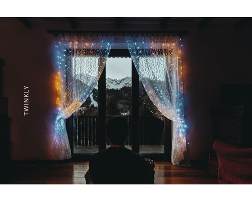 Osoba před oknem se světelným závěsem Twinkly a výhledem na hory