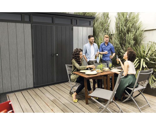 Zahradní scéna s domkem na nářadí a skupinou lidí, kteří společně jedí a pijí.