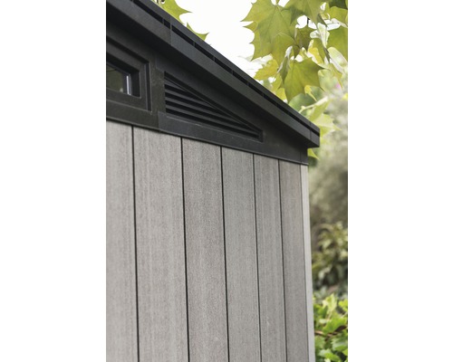 Detail zahradního domku s oknem a větrací mřížkou.