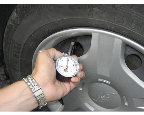 Osoba kontroluje tlak v pneumatikách pomocí měřiče tlaku v pneumatikách na pneumatice automobilu.