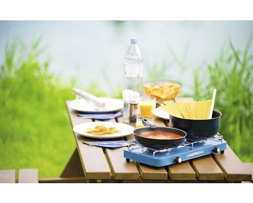 Kempingový stůl s vařičem, hrnec se špagetami a pánev s rajčatovou omáčkou pro jídlo venku