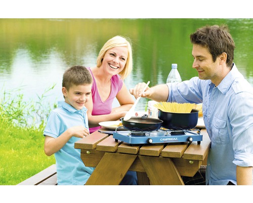 Rodina vaří s kempingovým vařičem u jezera.