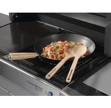 Plynový gril s wok pánví s krevetami a dvěma dřevěnými lžícemi.