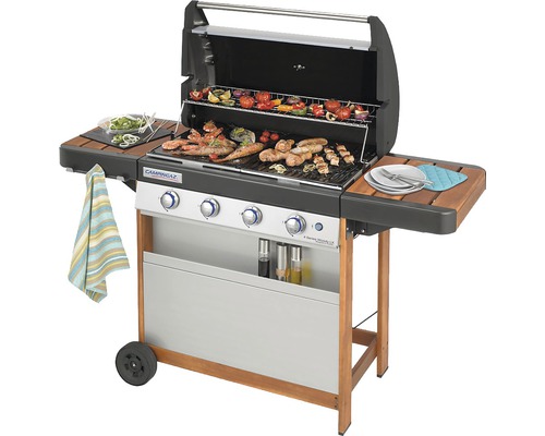 Plynový gril s jídlem na grilovací mřížce a dvěma bočními stolky.