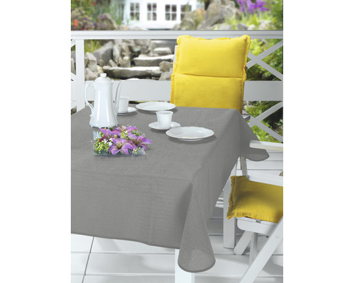 Ubrus na stůl zahradní PVC tmavě šedý 130 x 160 cm Prostřený zahradní stůl s šedým ubrusem, nádobím, kávovou konvicí, květinovou dekorací a žlutými polštáři na bílých zahradních židlích.