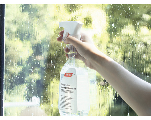 Osoba stříká montážní kapalinu na okenní fólie na okno.