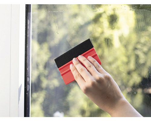 Ruka čistí okno stěrkou na okna.