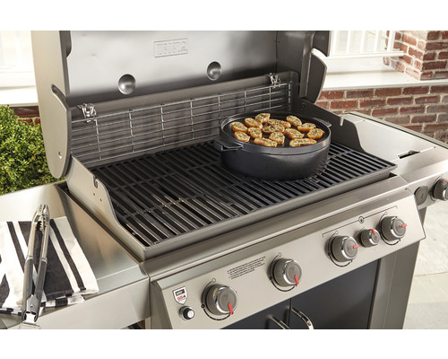 Nerezový gril s jídlem na grilovací desce a grilovacími kleštěmi