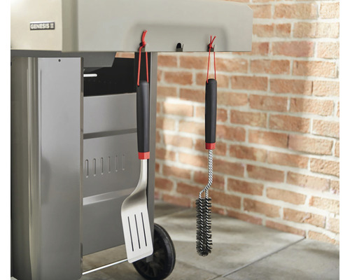 Grilovací náčiní a kartáč na gril zavěšené na grilu.