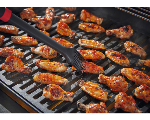 Kuřecí křídla se potírají štětcem na grilu.