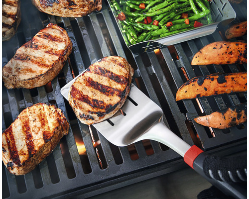 Na grilu jsou steaky, sladké brambory a zelené fazolky a steak se obrací grilovací obracečkou.