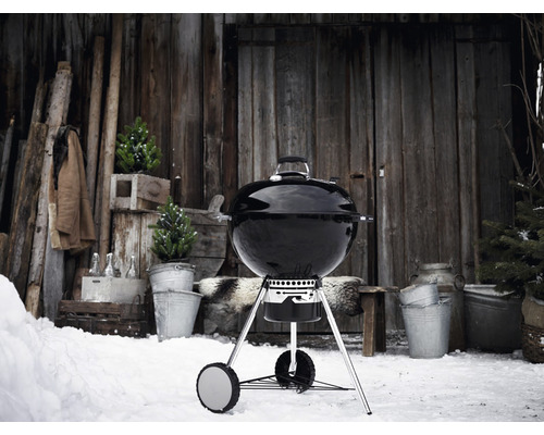 Kulatý gril ve sněhu před dřevěnou chatou