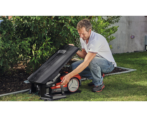 Muž otevírá víko robotické sekačky na trávu na zahradě.