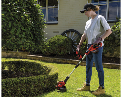 Žena používá akumulátorový vyžínač na zahradě.