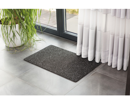 Šedá rohožka před dveřmi se závěsem a pokojovou rostlinou.