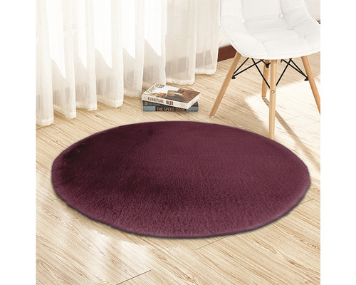 Kulový koberec s vysokým vlasem na dřevěné podlaze se židlí a knihami v pozadí.