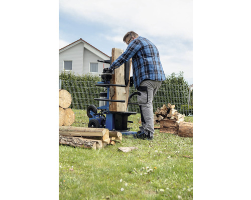 Muž štípe dříví štípačkou na dřevo na zahradě.