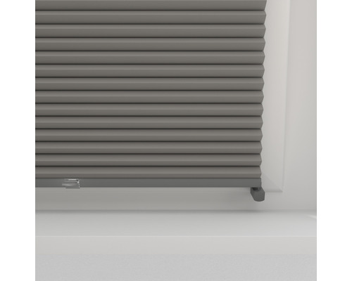 Detail šedé plisované žaluzie do okna pro regulaci světla a dekoraci