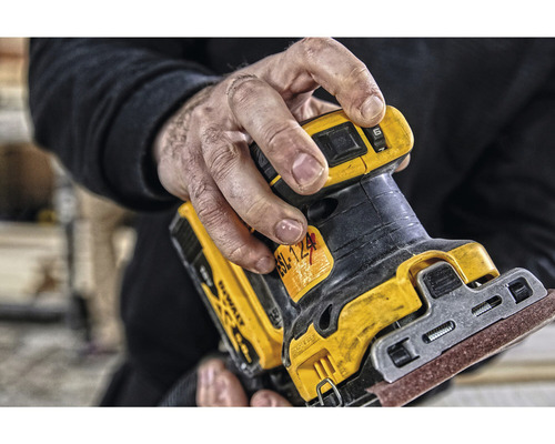 Detailní záběr muže držícího excentrickou brusku DeWalt.