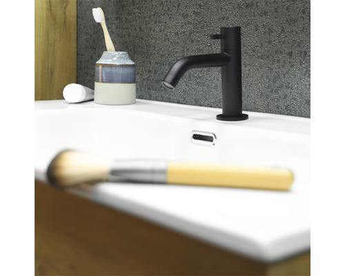 Černá umyvadlová baterie na bílém umyvadle se zubním kartáčkem, zubní pastou a štětcem na make-up