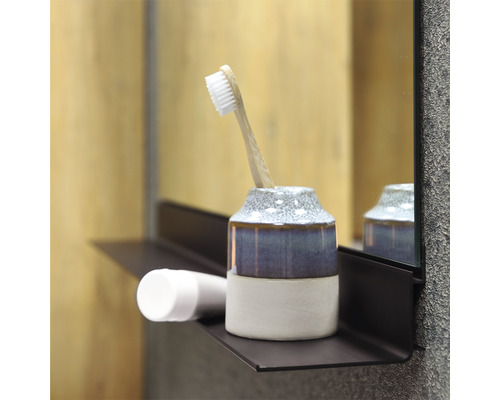 Koupelnová scéna s kelímkem na zubní kartáčky, zubním kartáčkem a kosmetickým produktem na polici