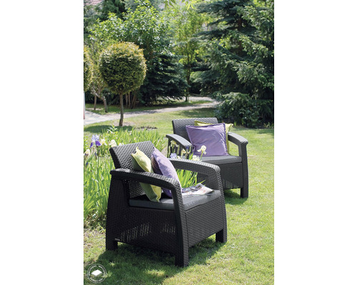 Dvě zahradní ratanová křesla s polštáři na zahradě.