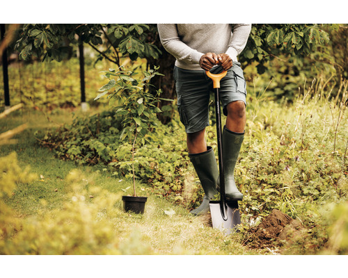 Osoba s rýčem sází strom na zahradě.
