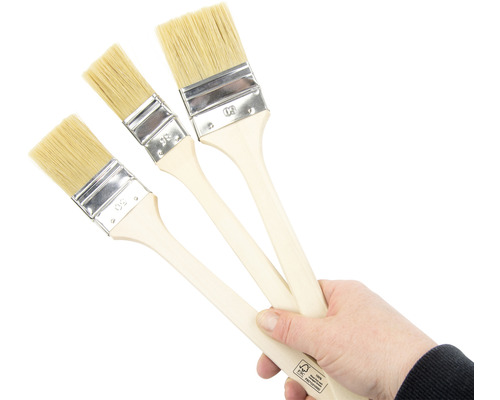 Ruka drží tři štětce s dřevěnými rukojeťmi a přírodními štětinami