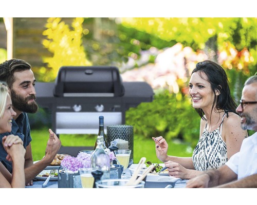 Zahradní scéna s lidmi u stolu a plynovým grilem