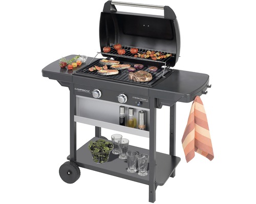 Plynový gril s grilovaným jídlem na roštu a odkládacími plochami.