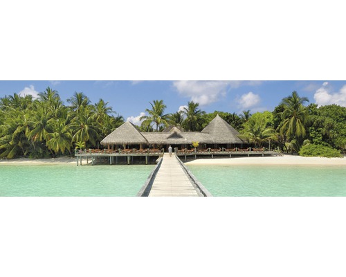 Panoramatický snímek resortu se střechami z došku, přístupného po mole z tyrkysové vody, obklopeného palmami.