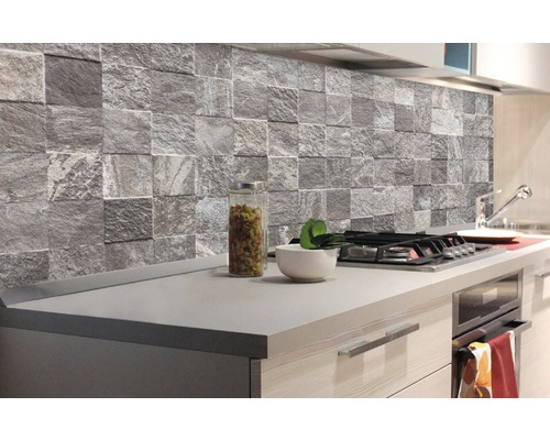 Kuchyňská scéna s šedými obkladovými panely z přírodního kamene nad pracovní deskou.