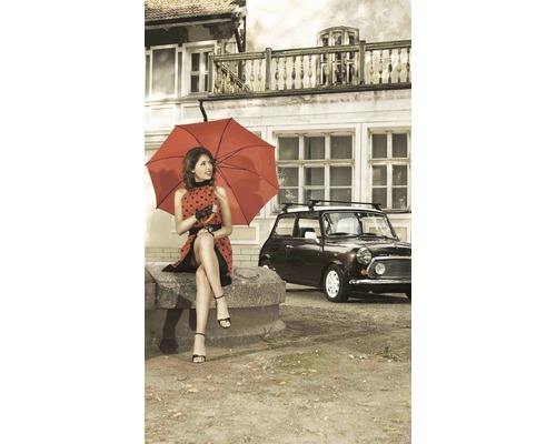 Žena s červeným deštníkem sedí před domem s autem v pozadí