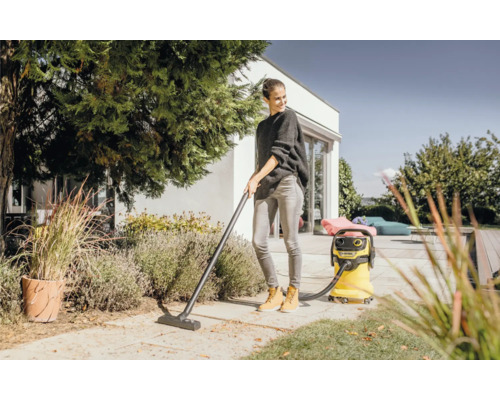 Žena používá žlutý víceúčelový vysavač Kärcher na zahradě k odstraňování listí