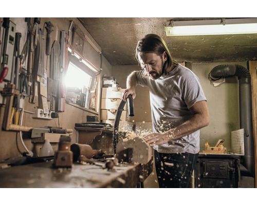 Muž uklízí ponk vysavačem v dílně