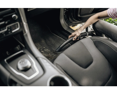 Osoba vysává interiér auta vysavačem.