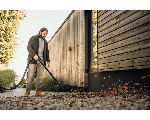 Muž odstraňuje listí pomocí vysavače listí před dřevěným domem.