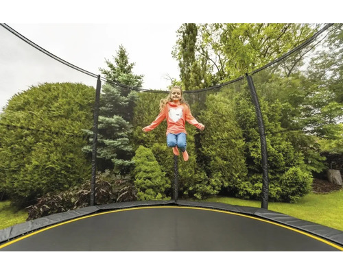 Dívka skáče na zahradní trampolíně se sítí před zelenými keři