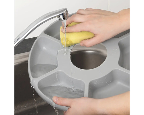 Osoba myje šedou mycí misku s přihrádkami pod kohoutkem houbou