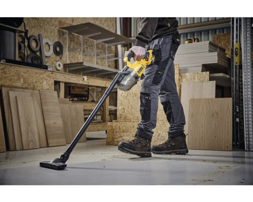 Pracovník používá akumulátorový vysavač DeWalt v dílně.