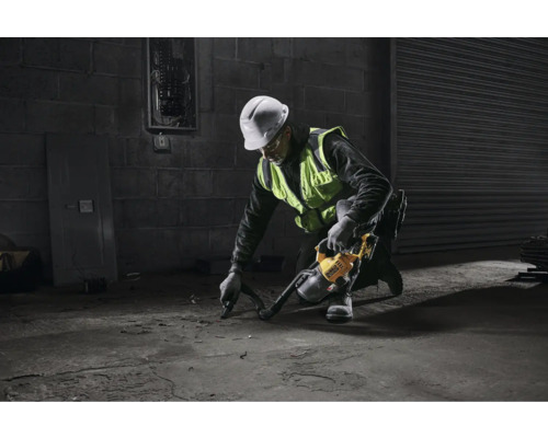 Muž s ochrannou helmou a výstražnou vestou používá průmyslový vysavač na betonové podlaze.