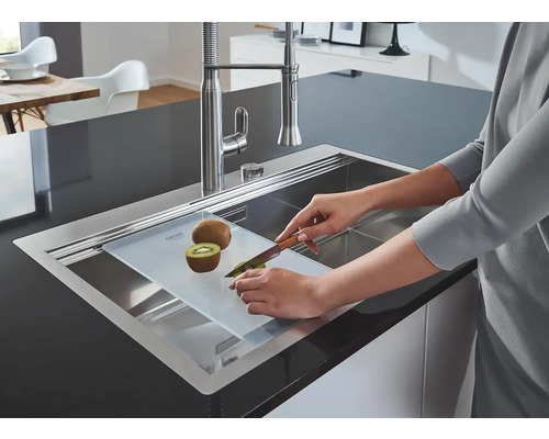 Nerezový dřez s krájecí deskou, na které osoba krájí kiwi