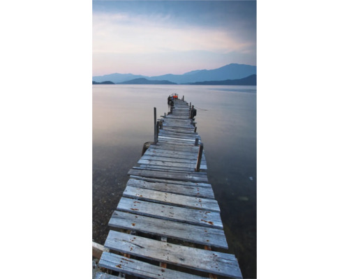 Dřevěné molo vede do klidné vody s horami v pozadí.