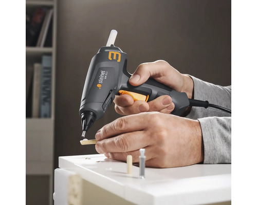 Osoba používá tavnou pistoli Steinel k lepení kusů dřeva na bílý povrch