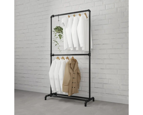 Černý kovový trubkový věšák na šaty s oblečením a rostlinou