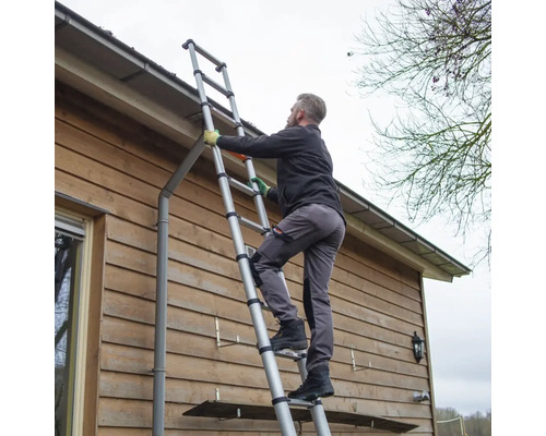 Osoba stoupá po teleskopickém žebříku u stěny domu.
