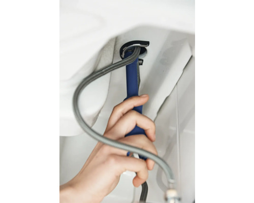 Řemeslník montuje vodovodní kohoutek pomocí nástroje a ohebné hadice.